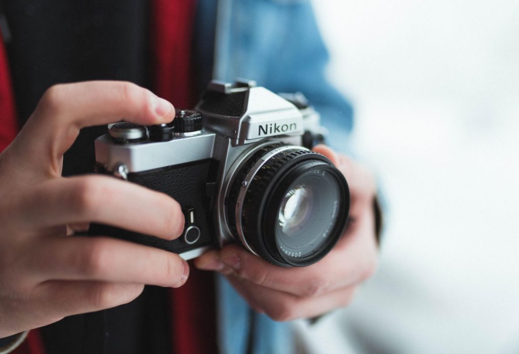 A Person Holding Up A Nikon Camera Up To His Chest