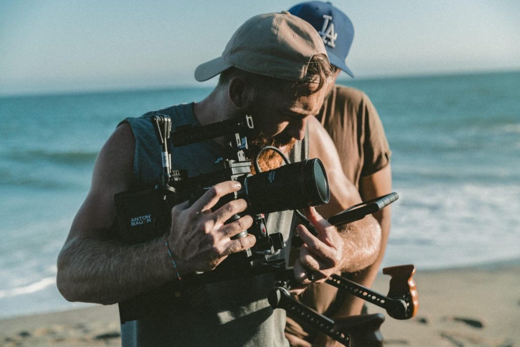 Two Guys Holding Up A Camera With Stabilizer